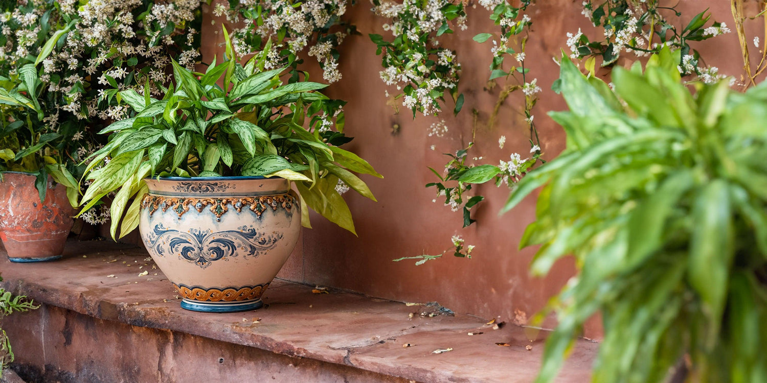 Cachepot ceramiche di Caltagirone fatti a mano con pianta verde su sfondo floreale