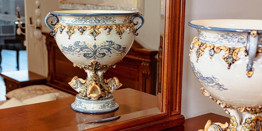 Ceramiche Caltagirone fatti a mano, vaso decorato con dettagli oro e blu su tavolo di legno riflesso in uno specchio