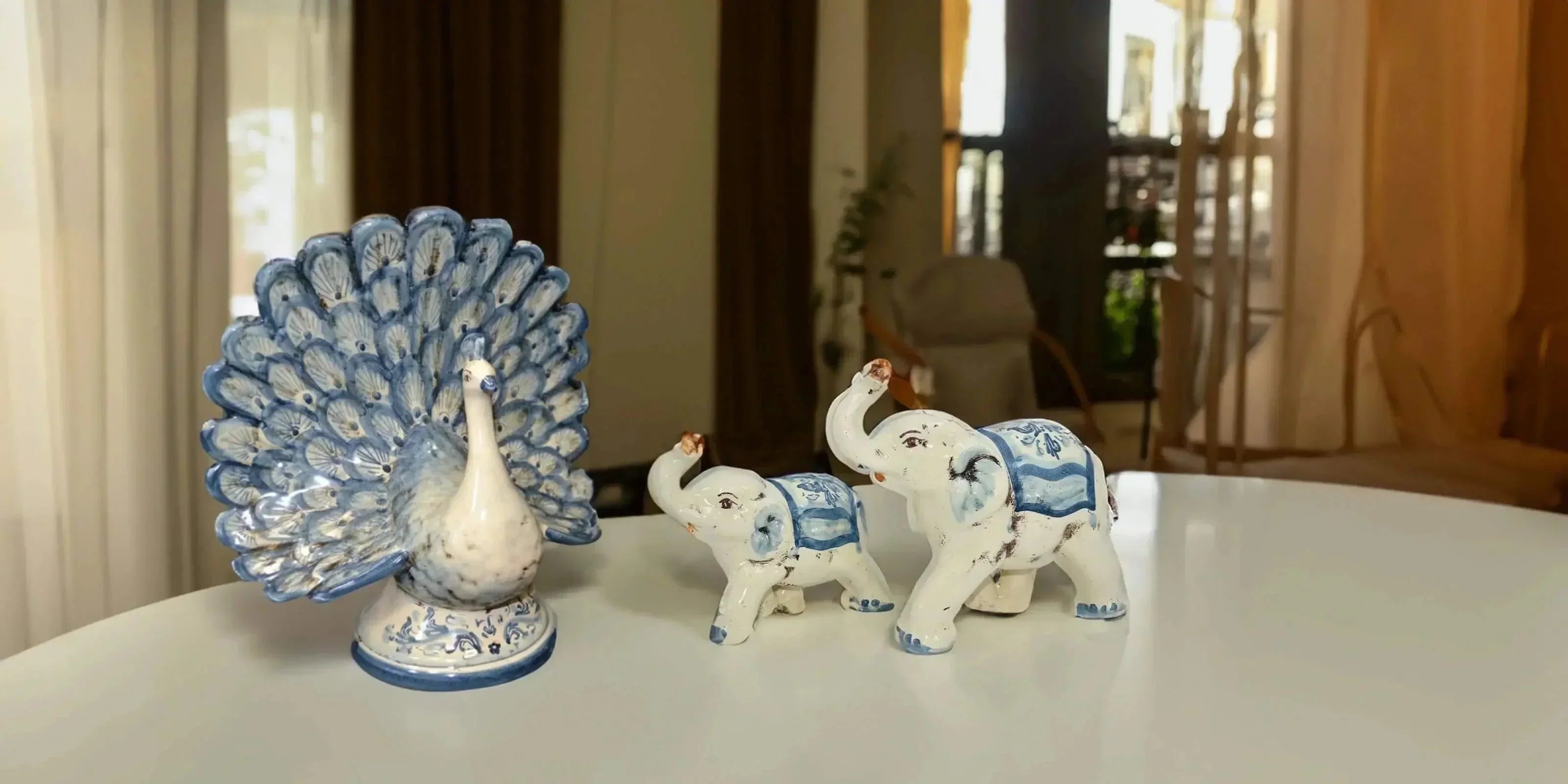 Animali in ceramica di Caltagirone fatti a mano, pavone e due elefanti bianchi e blu su tavolo bianco