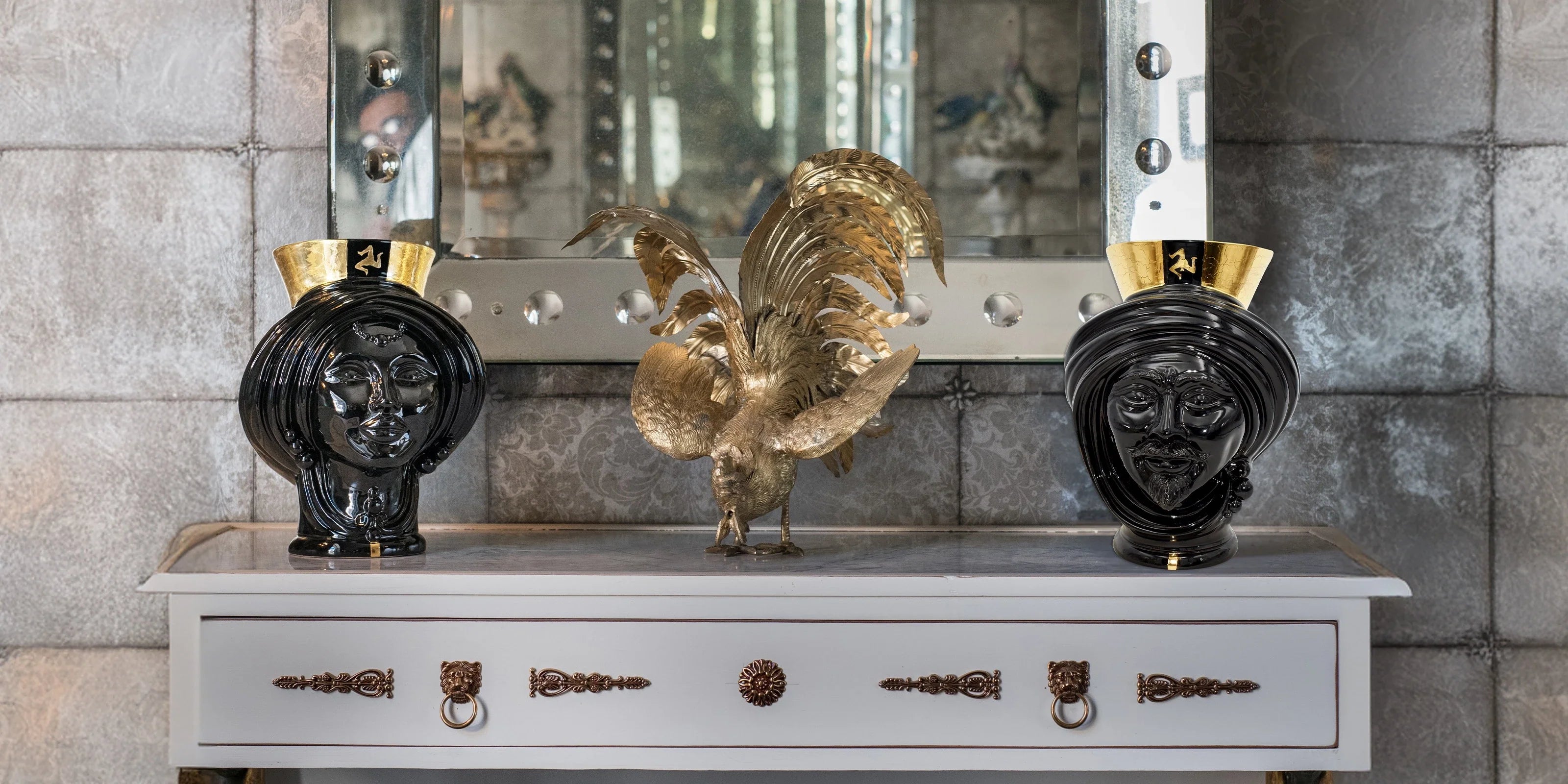 Ceramiche Caltagirone fatti a mano con teste nere lucide con dettagli dorati e scultura di gallo dorato su mobile bianco
