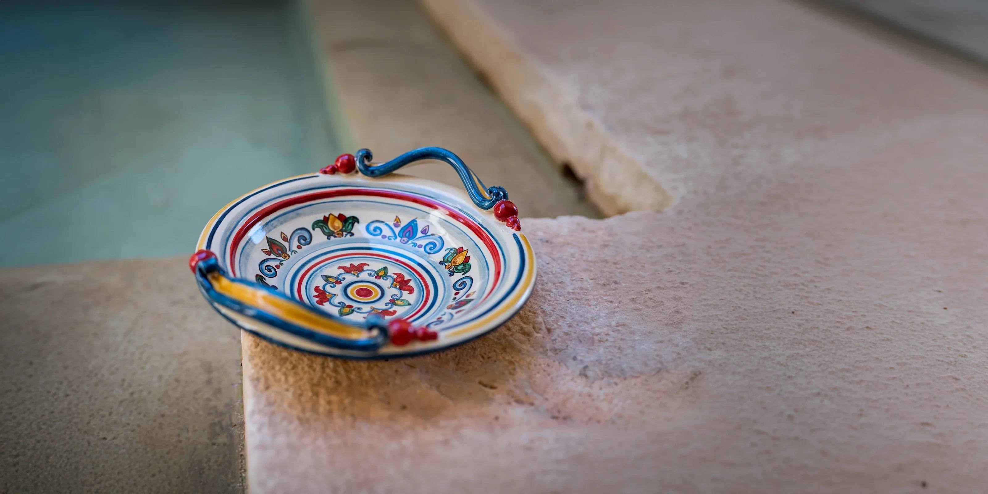 Piattino in ceramica di Caltagirone fatti a mano con decoro colorato, posato su bordo in pietra
