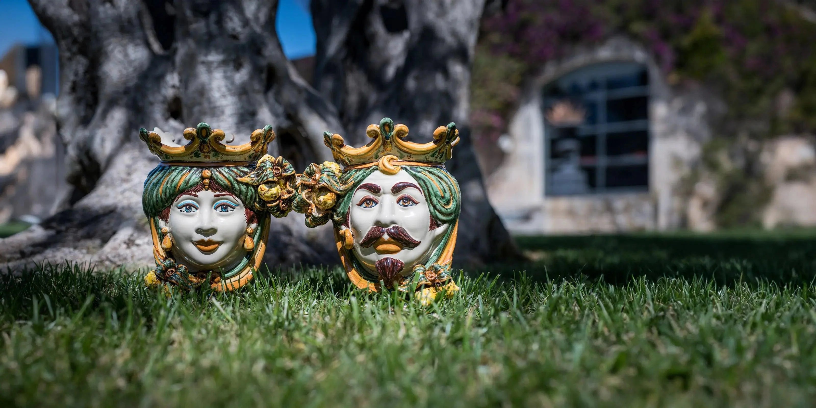 Testa di moro ceramiche Caltagirone fatte a mano in verde e arancio su prato davanti a albero