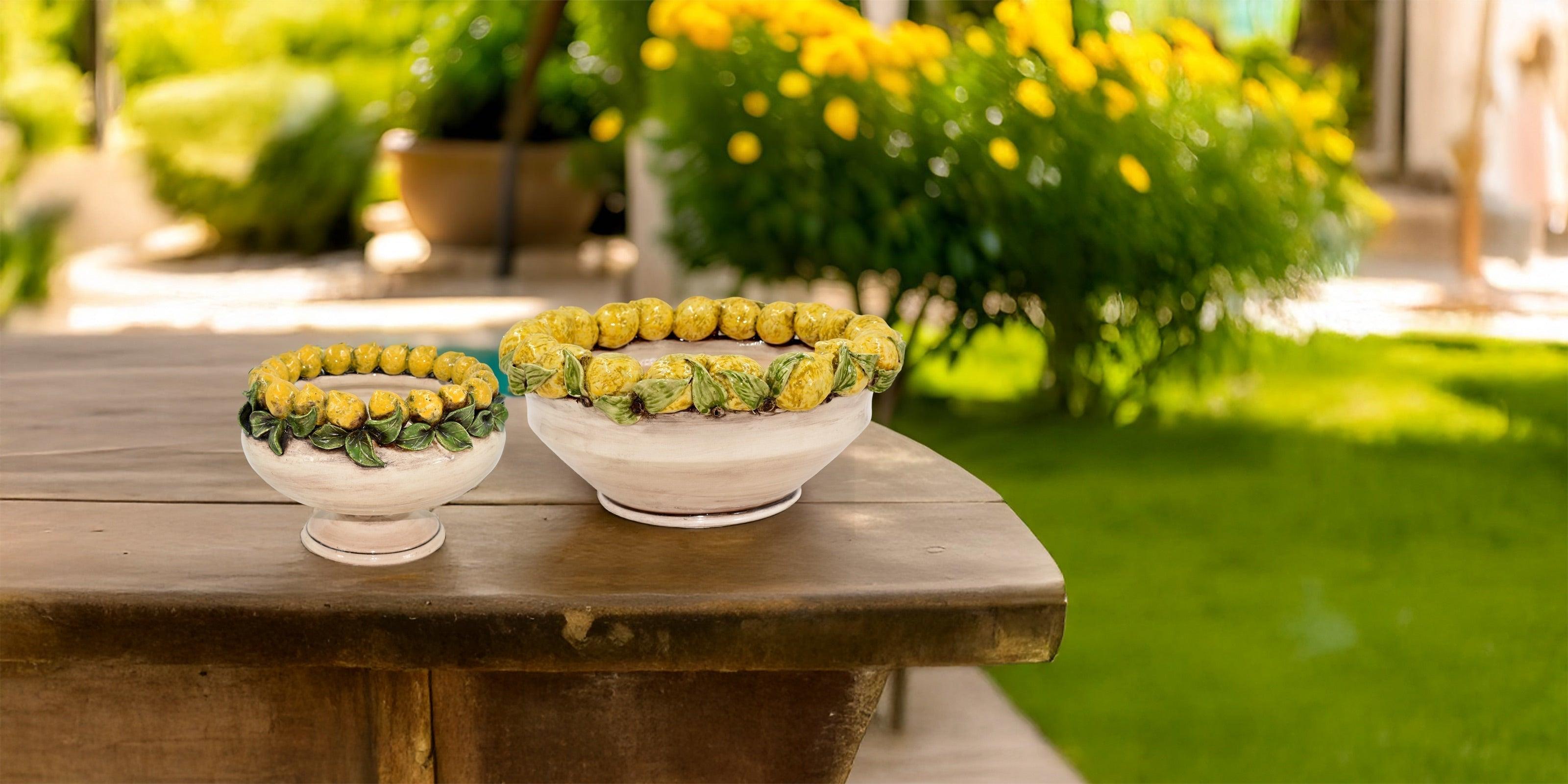 Due ciotole in ceramica di Caltagirone fatti a mano decorate con limoni gialli e foglie verdi posate su tavolo di legno in giardino