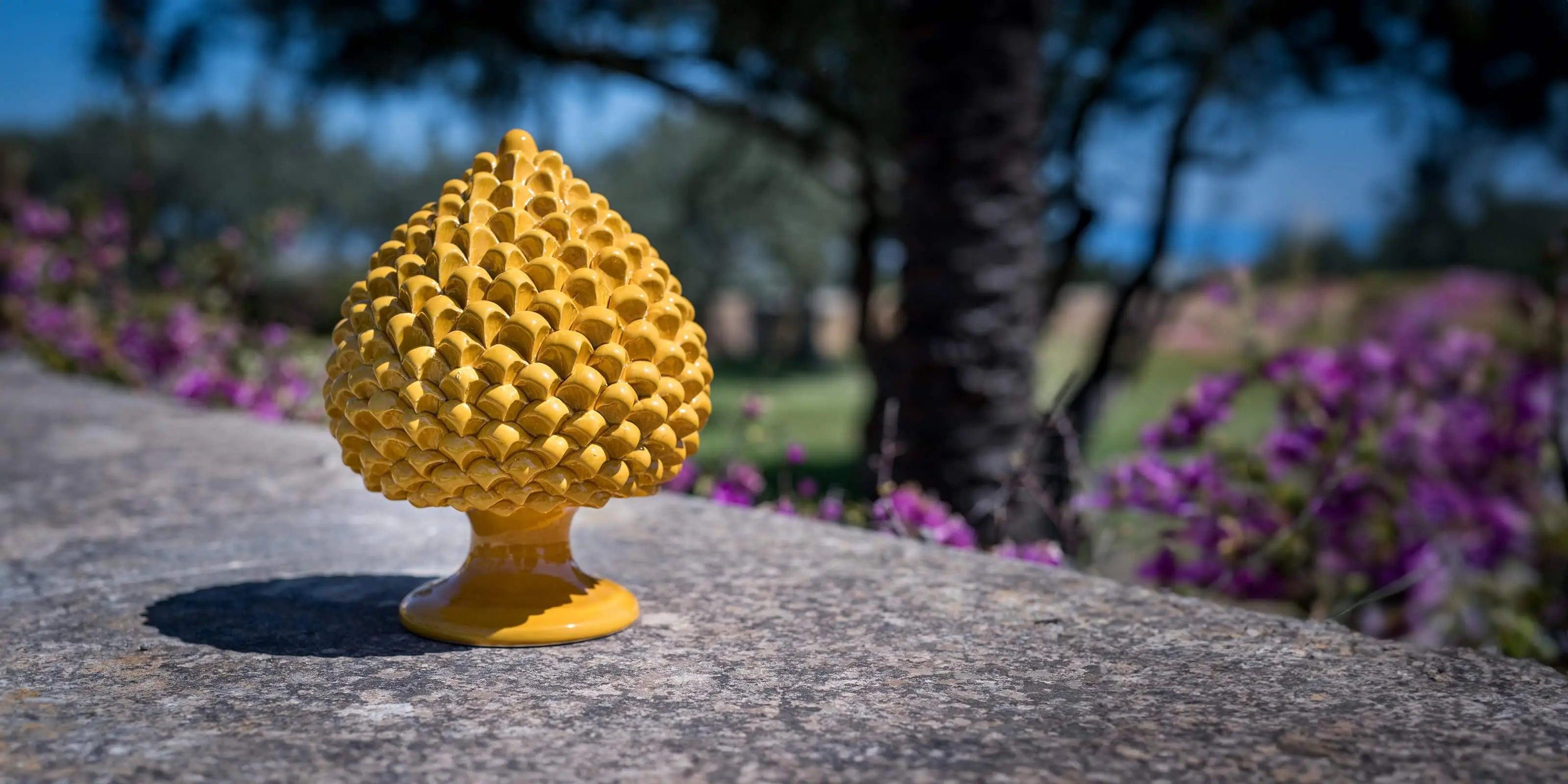 Pigna in ceramica gialla fatta a mano su muro esterno con sfondo flou di fiori e alberi ceramiche caltagirone fatti a mano