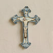 Crucifijo de cerámica de Caltagirone Mono Azul colgado en una pared clara, hecho a mano con Cristo en relieve y volutas pintadas en azul
