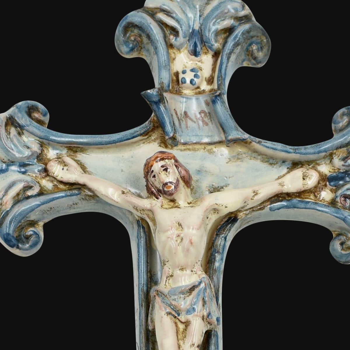 Detalle del crucifijo de cerámica de Caltagirone Mono Azul: Cristo en relieve, cartela INRI y remate con volutas pintadas a mano en azul