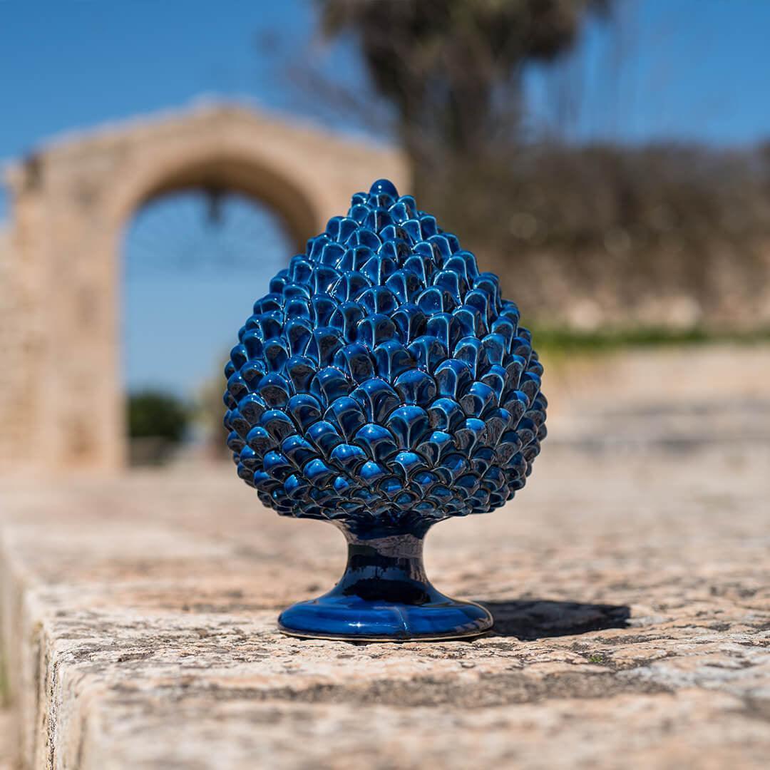 Pigna artigianale di Caltagirone in ceramica blu intenso, fatta a mano, su muro in pietra con arco sfocato