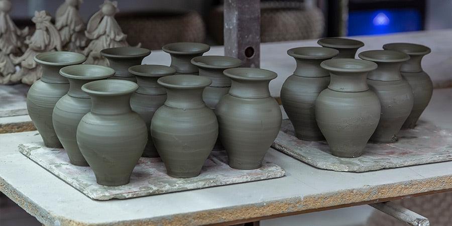 Vasi in argilla freschi, ceramiche Caltagirone fatti a mano su piano di lavoro artigianale.