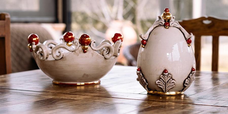 Ceramiche di Caltagirone fatti a mano, ciotola e vaso decorativi in ceramica bianca con dettagli rossi e dorati su tavolo in legno