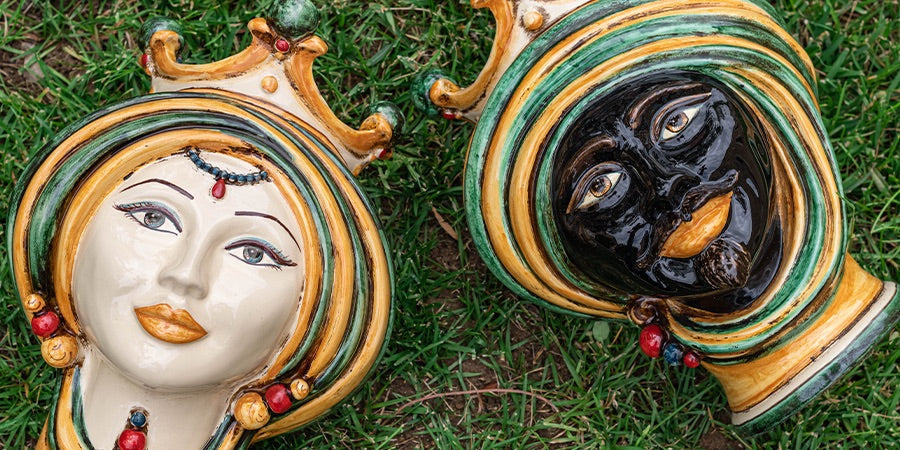 Teste di Moro ceramiche di Caltagirone fatti a mano con dettagli oro e colori verde, bianco e nero posate su erba