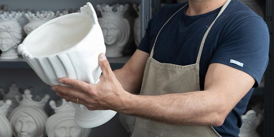 Artigiano con grembiule che tiene ceramica bianca fatta a mano di Caltagirone