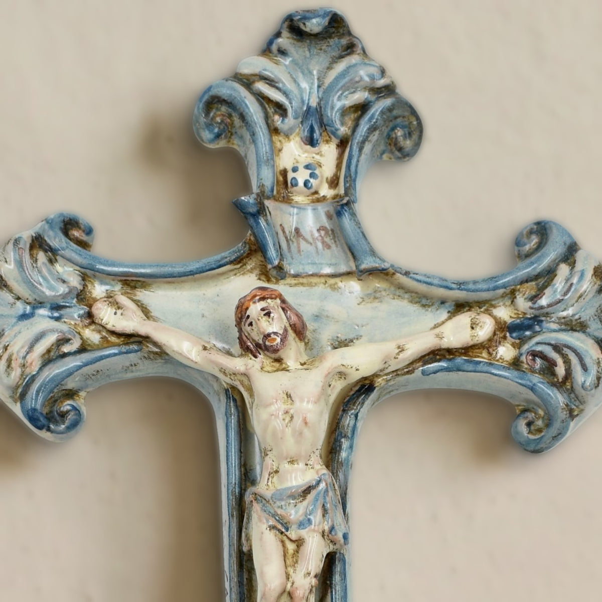 Détail du crucifix en céramique de Caltagirone Mono Bleu au mur : Christ en relief, cartouche INRI et cimaise à volutes bleues